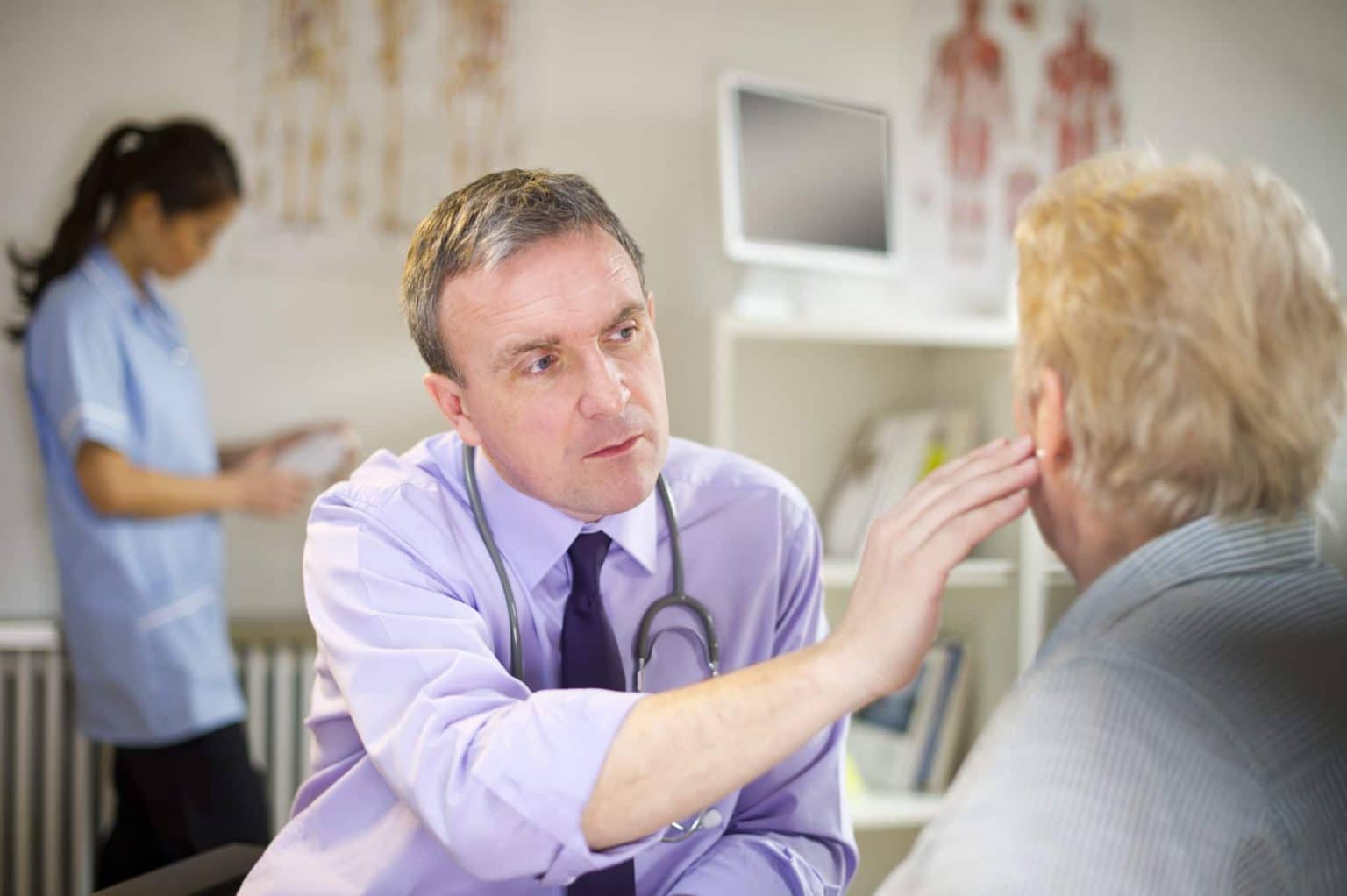 ENT Diagnosing Earwax Removal ENT is holding his hand against a patients ear as he discusses symptoms related to earwax pain that may require removal.